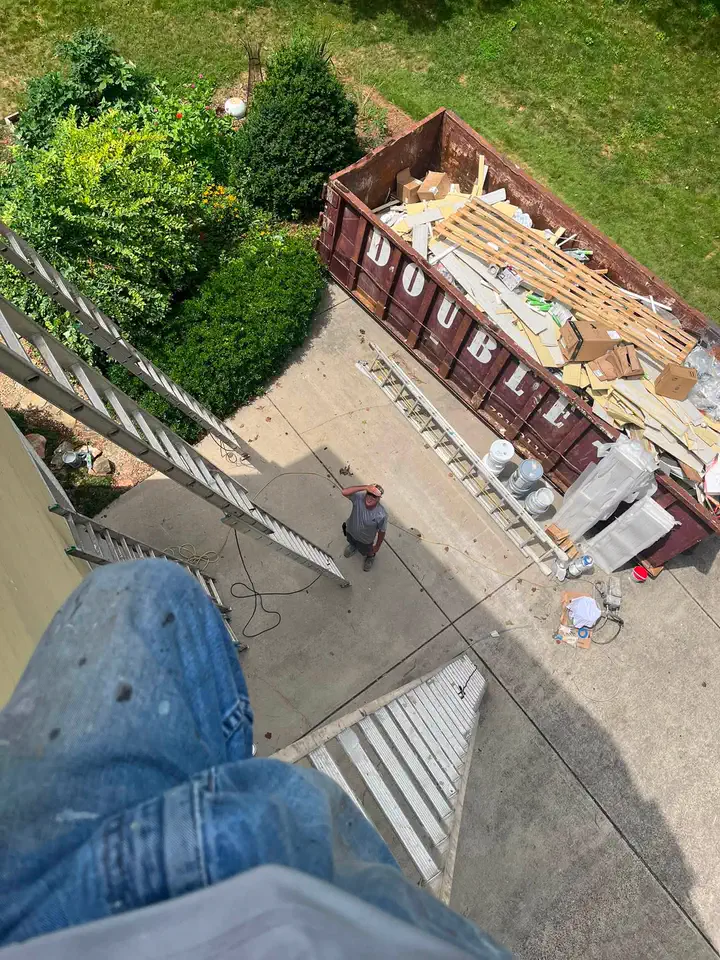 Upper exterior wall being prepared and painted from a ladder
